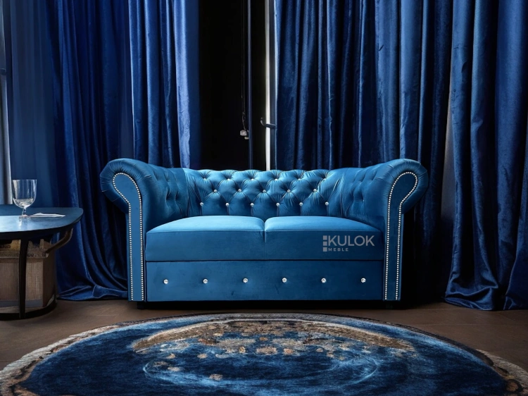 Chesterfield dwuosobowa sofa z funkcją spania, niebieska, pikowana z dekoracyjnymi srebrnymi detalami, wykonana z miękkiego weluru.