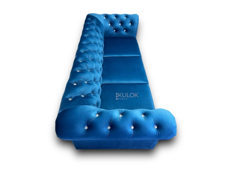Niebieska sofa w stylu glamour, pikowana, z funkcją spania i ozdobnymi kryształkami.