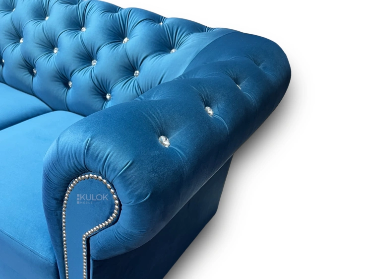 Niebieska sofa w stylu glamour, pikowana, z funkcją spania i ozdobnymi kryształkami.